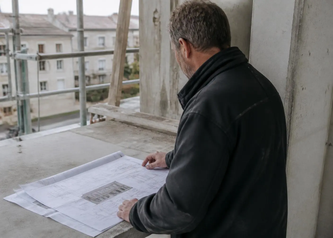 Responsable de obra revisando planos impresos sobre una losa de hormigón